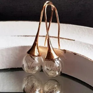 Close-up of transparent glass ball earrings with dandelion seed inside on silver French hook
