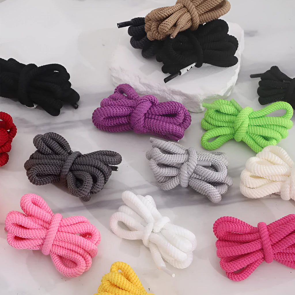 Oval cross-section shoelace adapter rope in various colours, shown next to a trainer and sweatshirt.