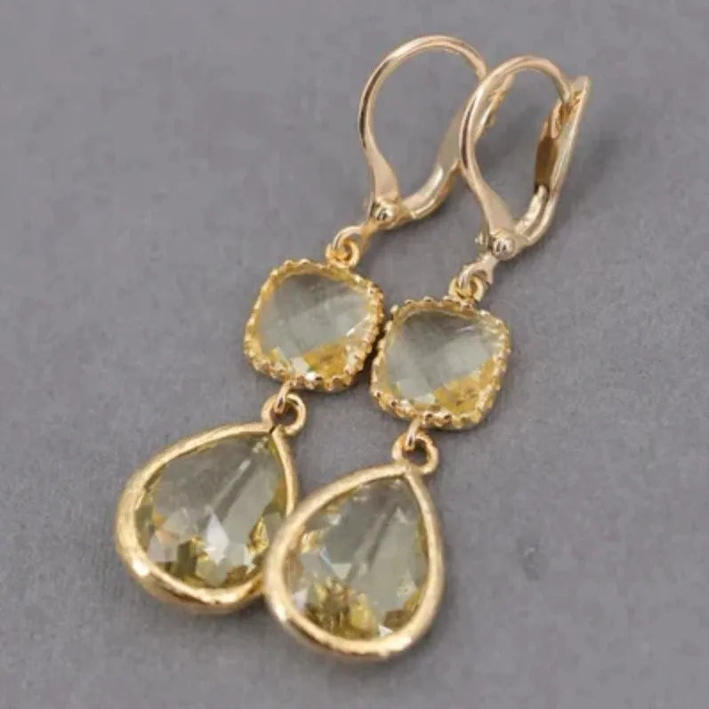 Gold long drop earrings with geometric shape and water droplet crystal fringe on a model.