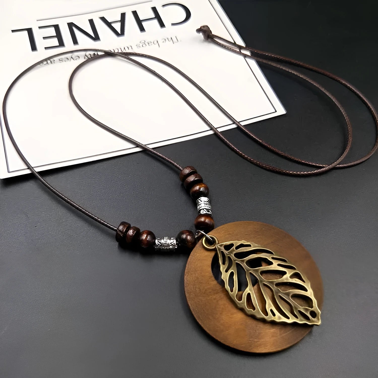 Wooden leaf pendant necklace with wax-line chain on a neutral background.