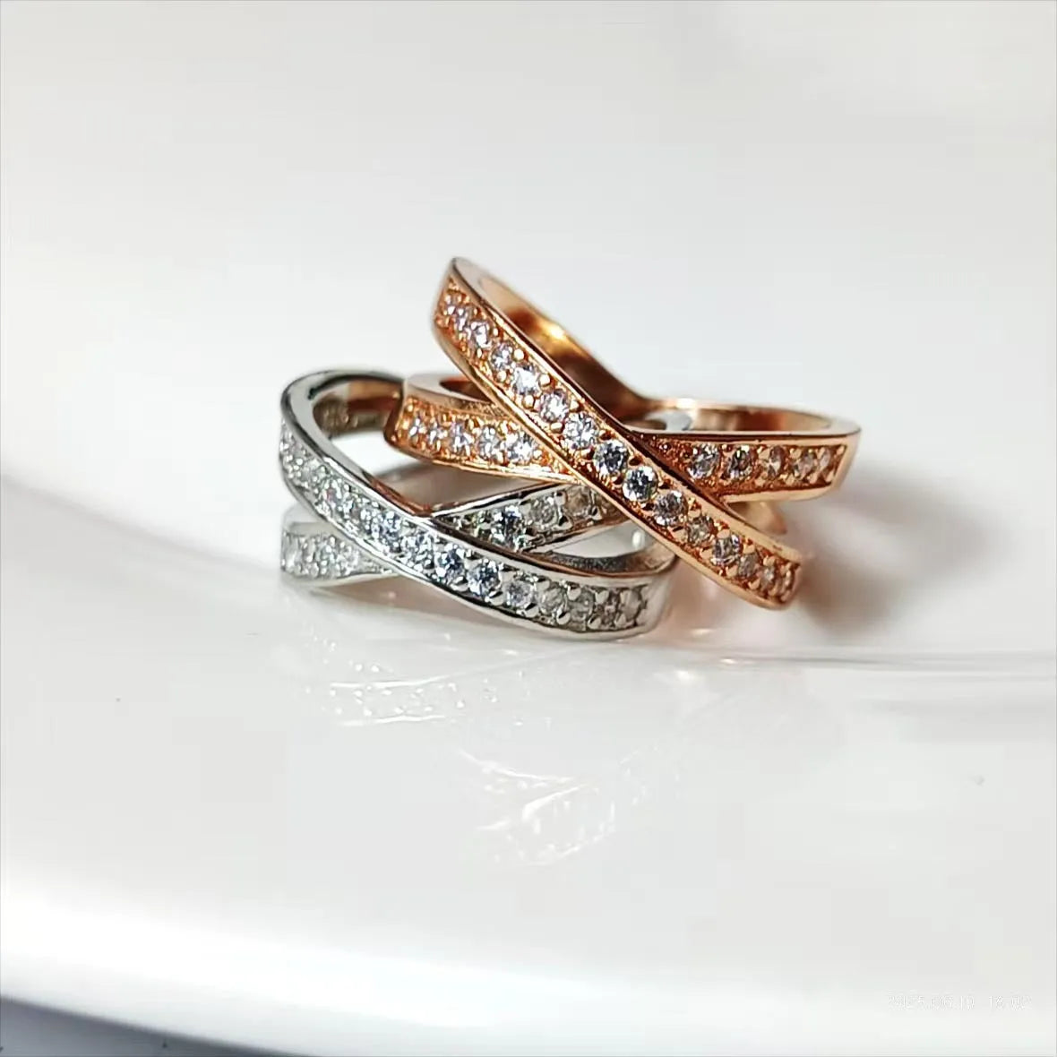 Simple metal cross ring with micro-inlaid zircon on a geometric band, shown in silver and rose gold finishes.