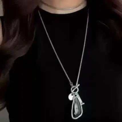 Long geometric alloy pendant necklace with snake bones chain for wearing over sweaters.