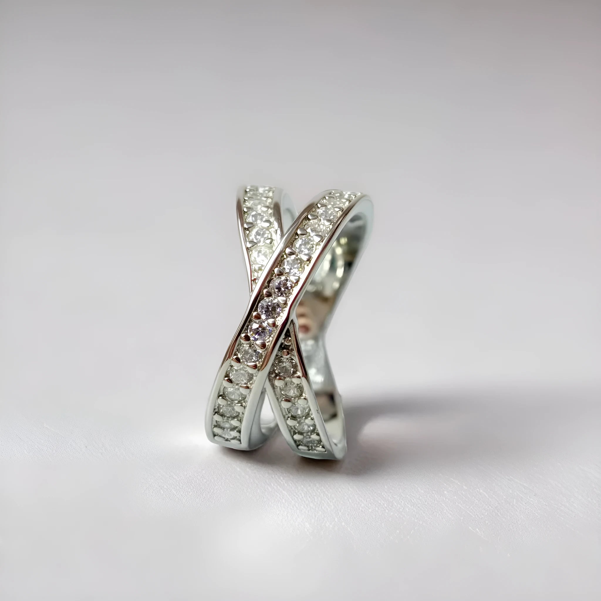 Simple metal cross ring with micro-inlaid zircon on a geometric band, shown in silver and rose gold finishes.
