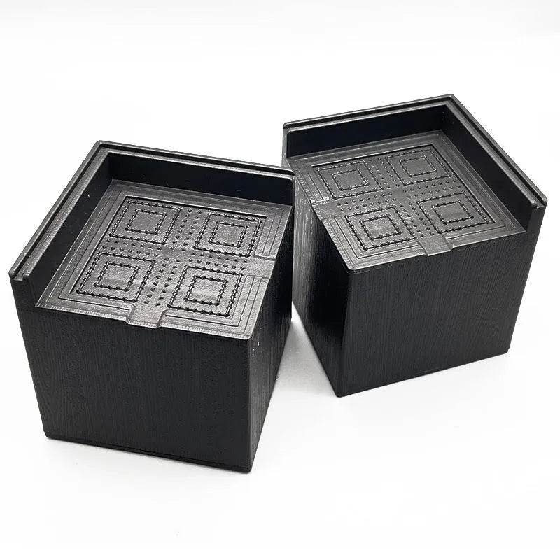 Four black thickened plastic furniture foot height increasing mats on a white background