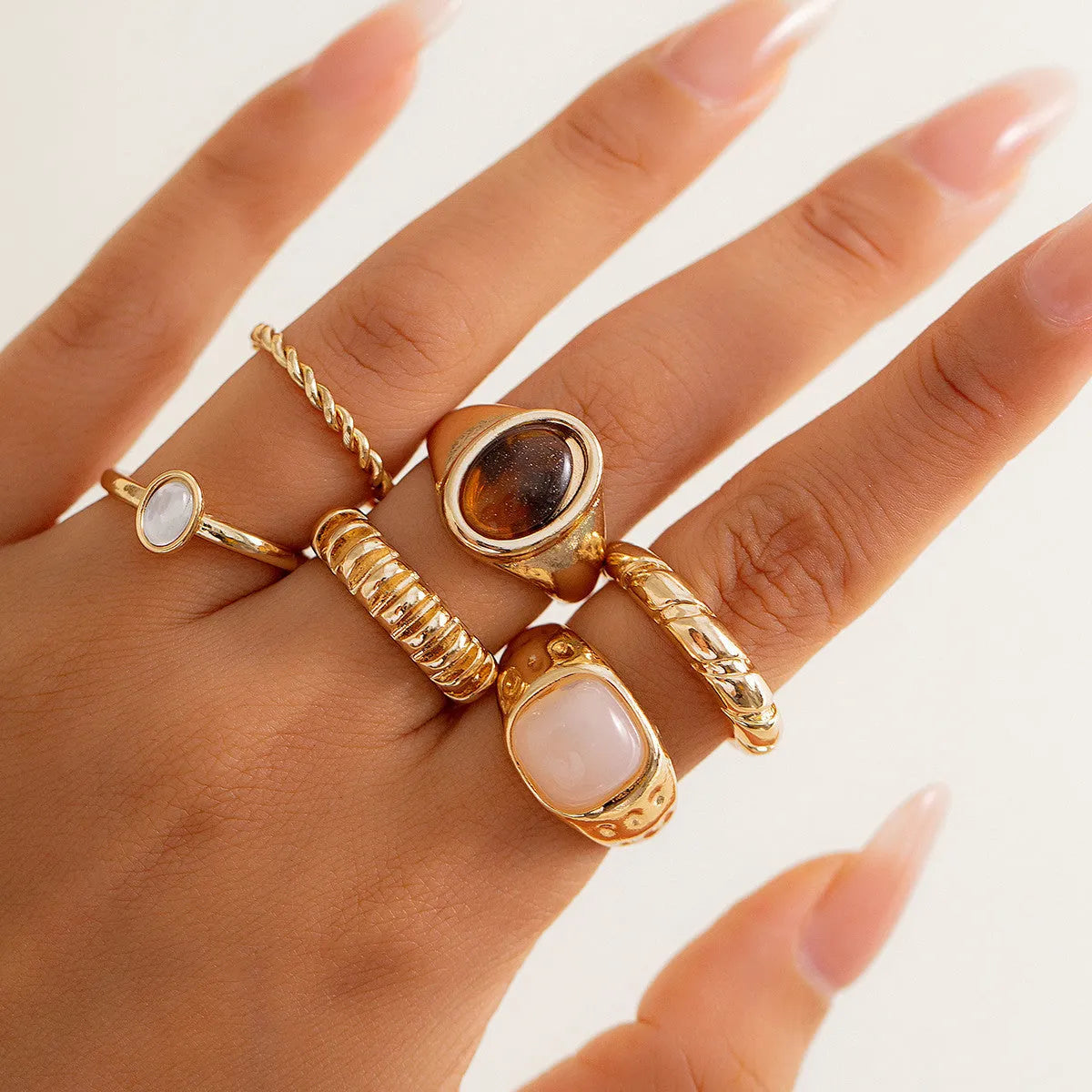 Six light gold alloy rings with geometric shapes and round elements arranged as a complete ring suit