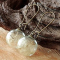 Close-up of transparent glass ball earrings with dandelion seed inside on silver French hook