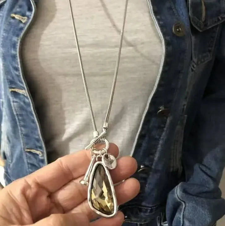 Long geometric alloy pendant necklace with snake bones chain for wearing over sweaters.