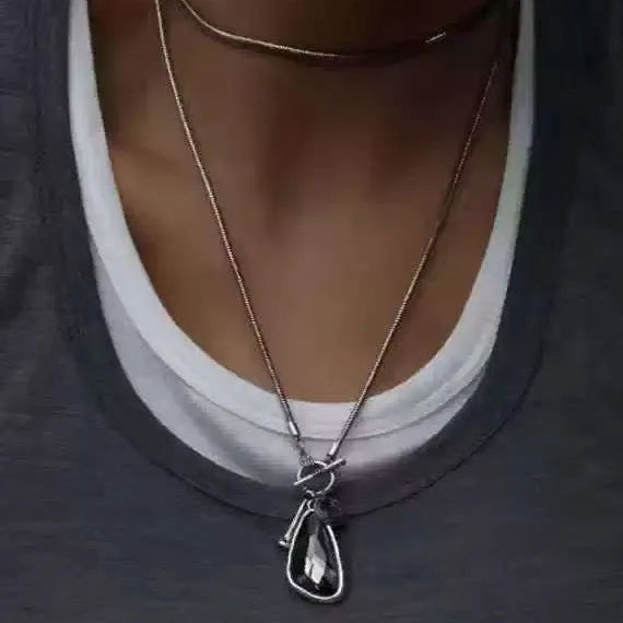 Long geometric alloy pendant necklace with snake bones chain for wearing over sweaters.