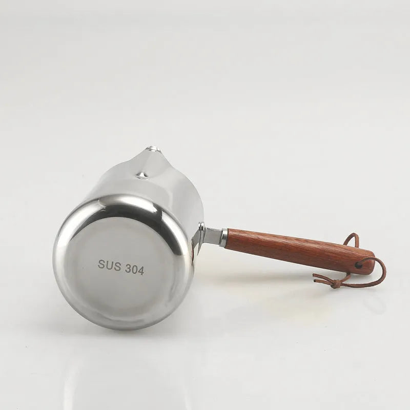 Stainless steel latte art milk cup with wooden handle and visible internal measurement scale.