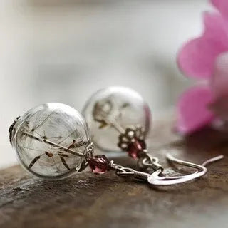 Close-up of transparent glass ball earrings with dandelion seed inside on silver French hook