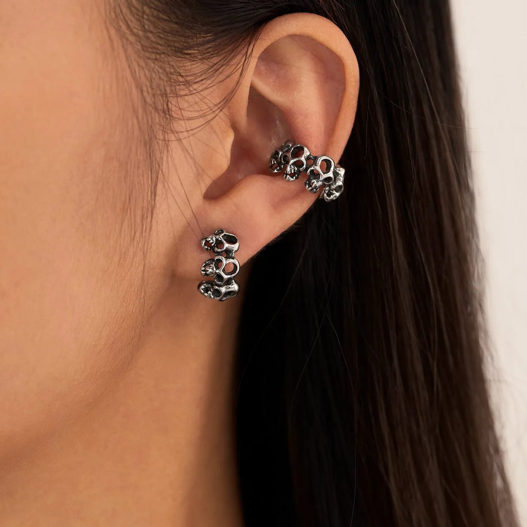 Stainless steel clip-on earrings featuring a hollow geometric skull design with an electroplated finish.