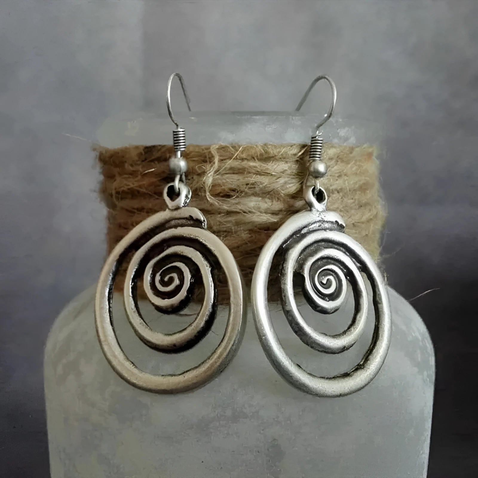 Geometric spiral distressed silver alloy drop earrings on a white background.
