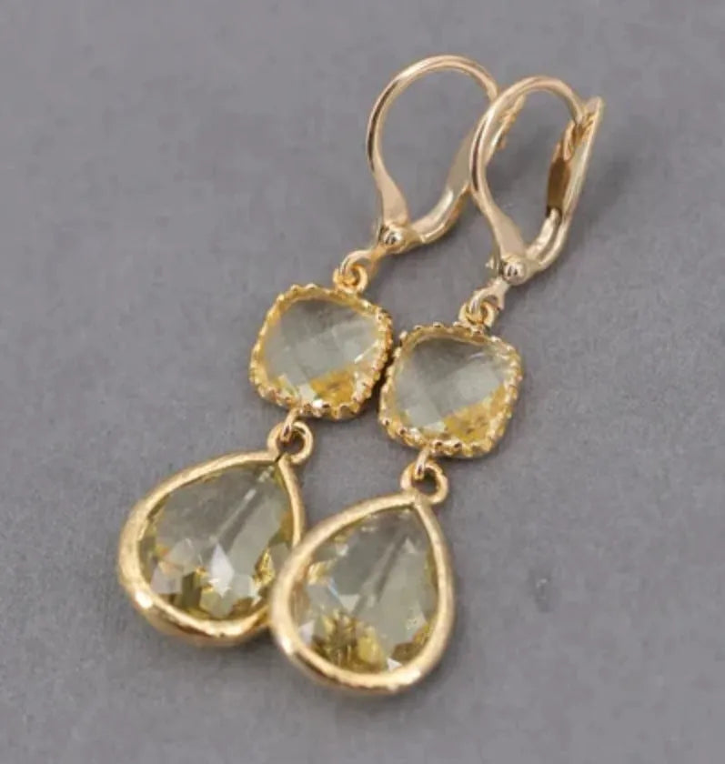 Gold long drop earrings with geometric shape and water droplet crystal fringe on a model.