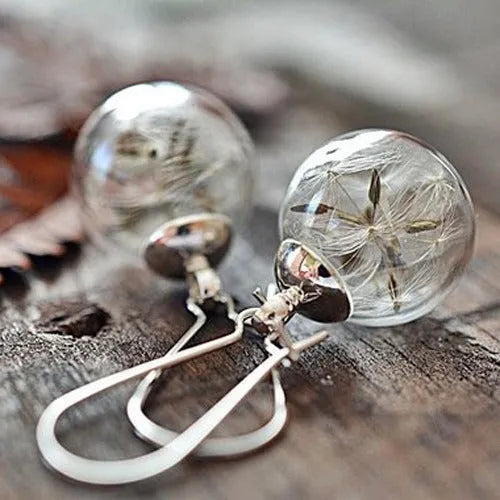 Close-up of transparent glass ball earrings with dandelion seed inside on silver French hook