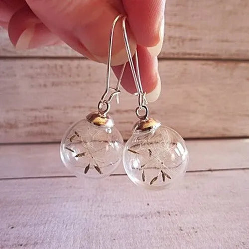 Close-up of transparent glass ball earrings with dandelion seed inside on silver French hook
