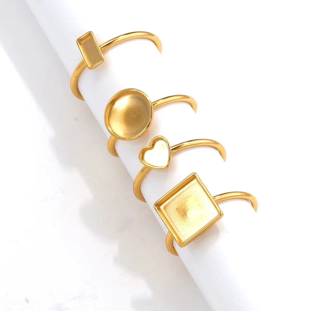 Assortment of golden stainless steel DIY jewellery settings in oval, heart, round, square, and rectangle shapes with totem pattern.