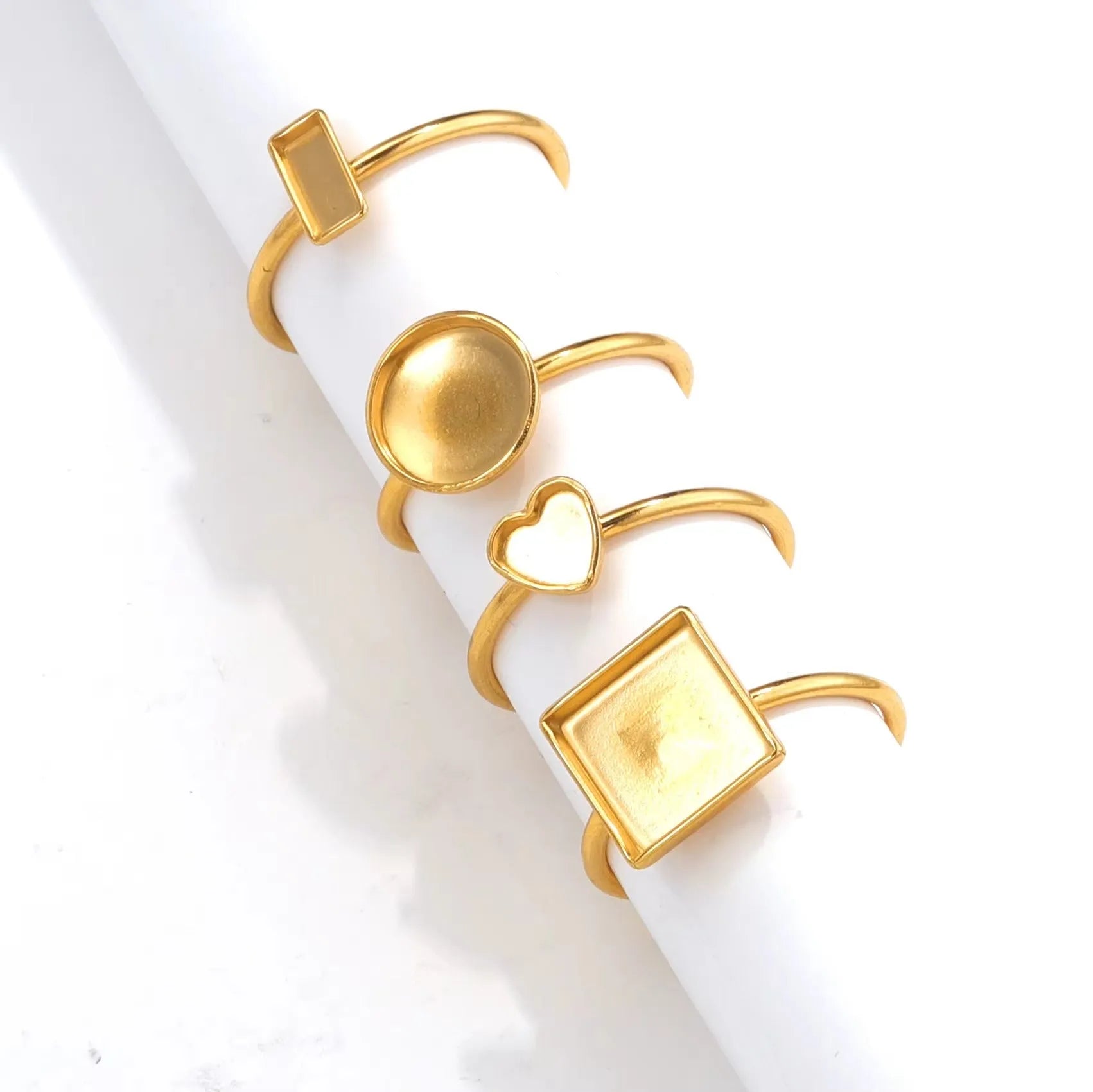 Assortment of golden stainless steel DIY jewellery settings in oval, heart, round, square, and rectangle shapes with totem pattern.