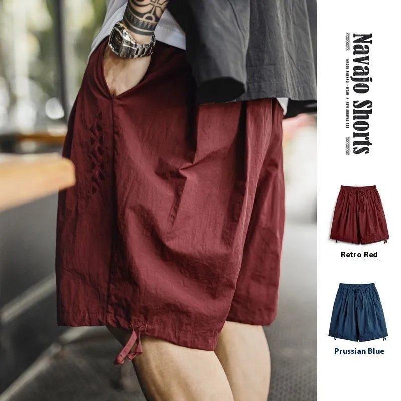 Prussian blue men's loose-fit nylon shorts with embroidery on a summer beach background.