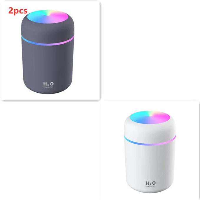 Pink USB desktop humidifier with LED lights and water tank on a wooden desk.