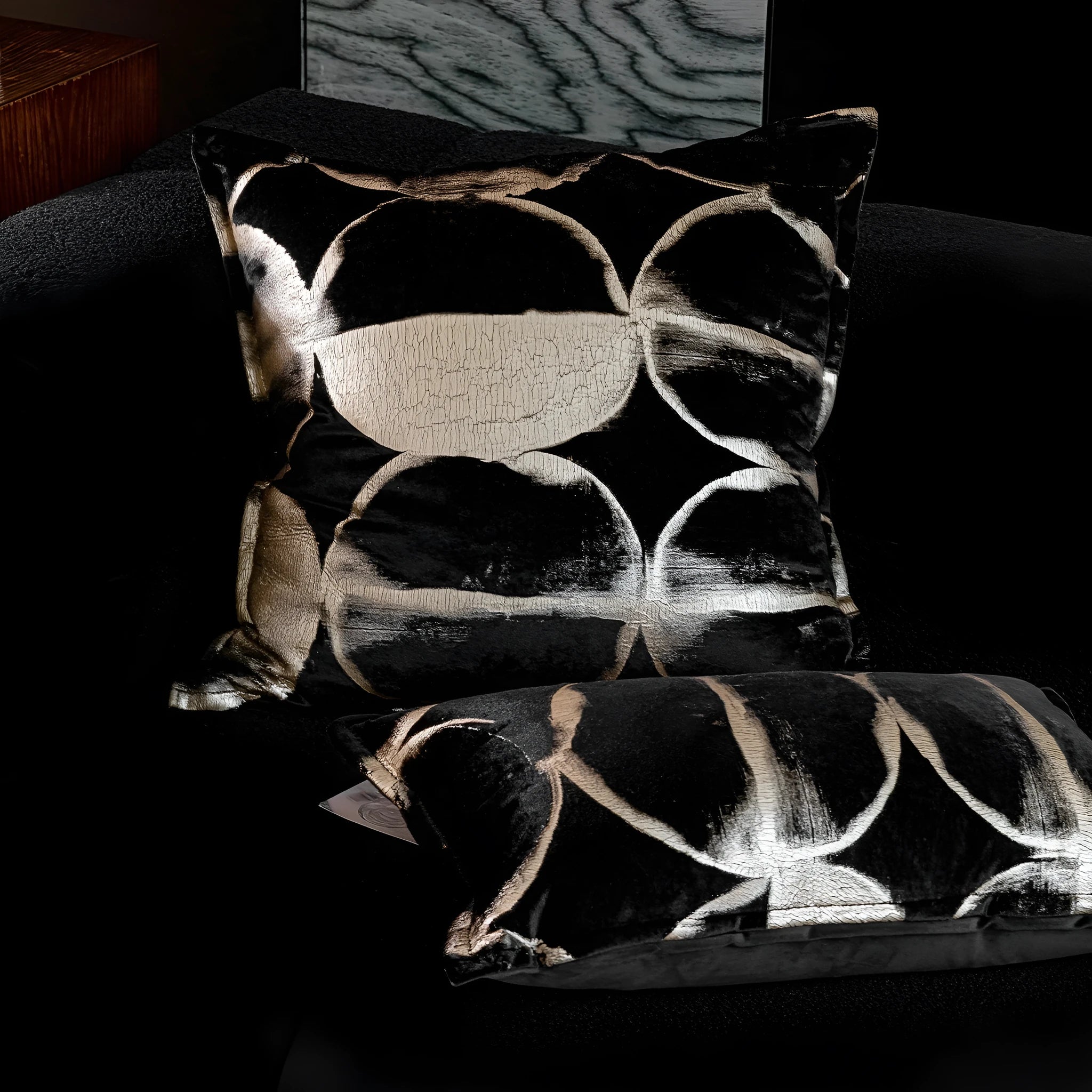 Black and gold abstract pattern decorative velvet cushion on a grey sofa.