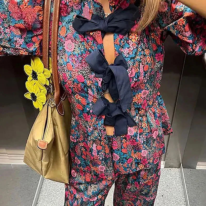 Women's floral print trousers suit with tie-neck puff sleeve top and matching trousers.
