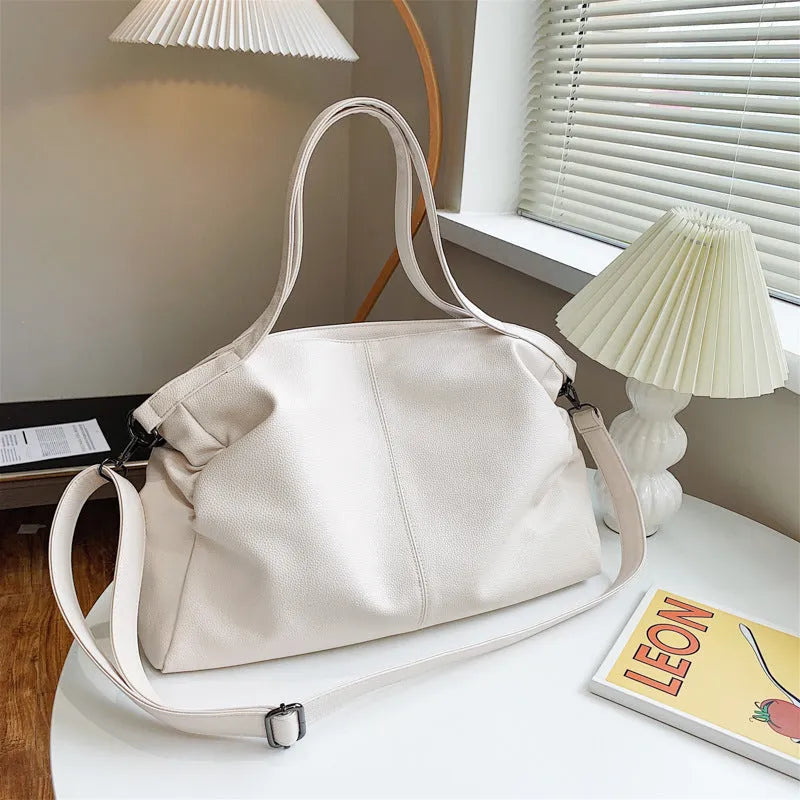 Large soft surface black messenger bag with soft handle and long shoulder strap on a table