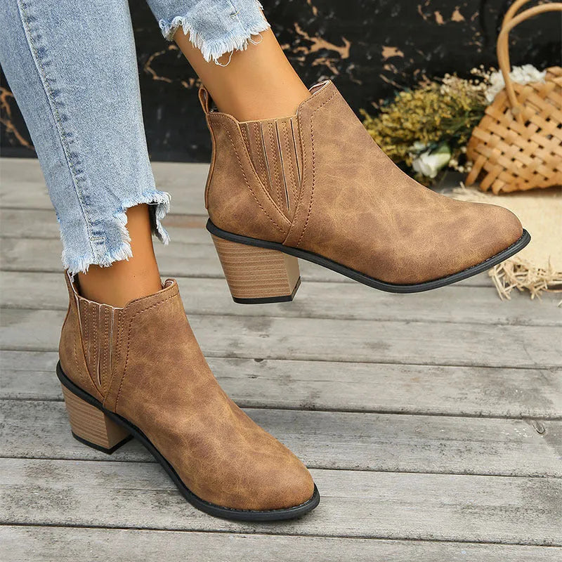 Women's black ankle boots with pointed toe and thick square heel on wooden floor