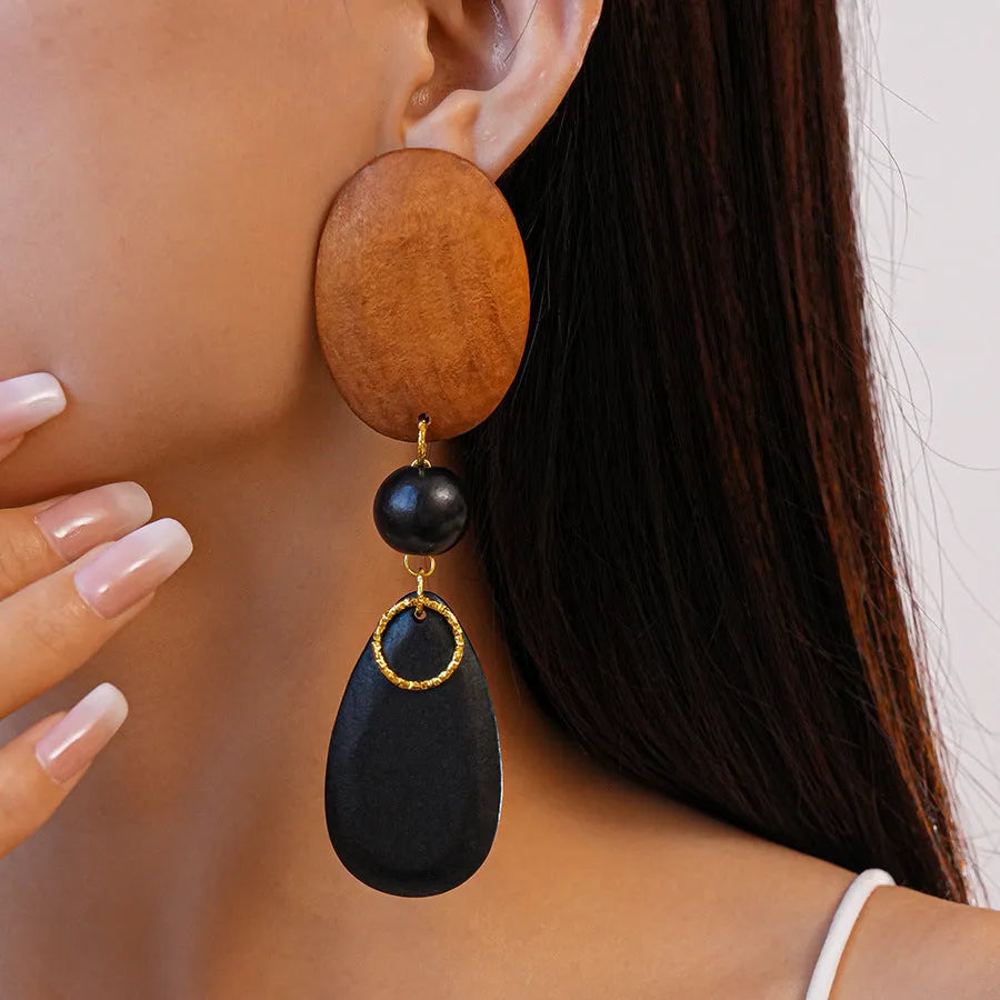 Handmade brown and black wooden ellipse earrings with silver needle fastenings on a white background.