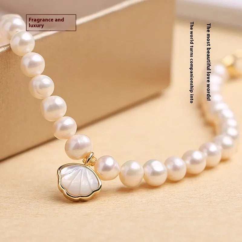 Women's freshwater pearl bracelet with fan-shaped charm on wrist, showing elastic and chain fastening options.