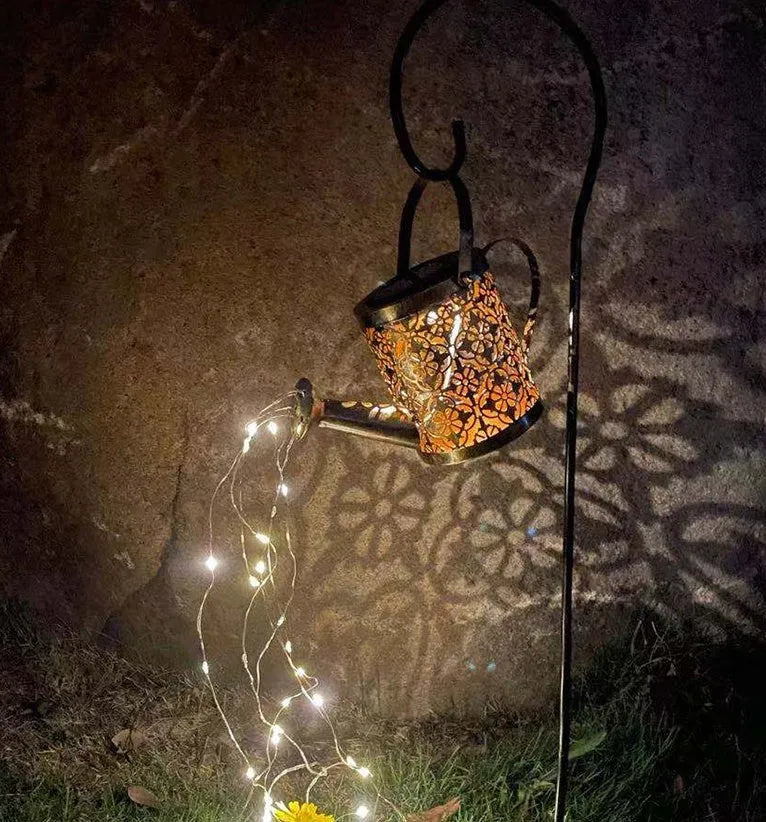 Enchanted watering can solar lamp with warm white star-shaped LED lights in a garden setting
