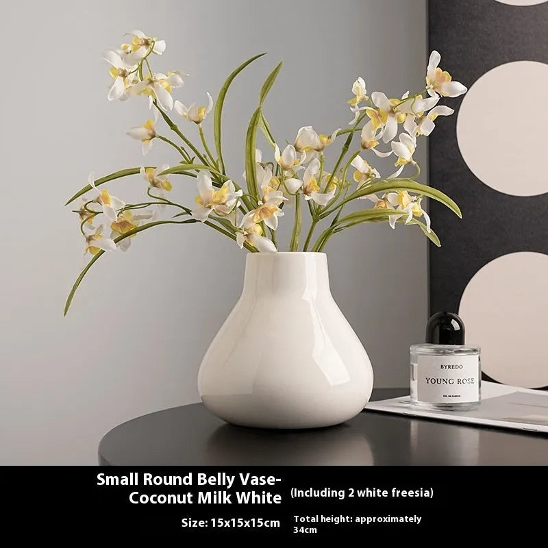 Black ceramic round belly vase with white artificial orchids on wooden table