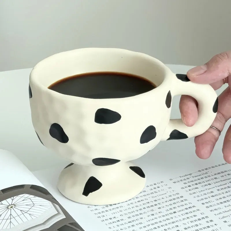 Hand-pinched irregularly shaped ceramic mug in a solid colour, shown on a table.