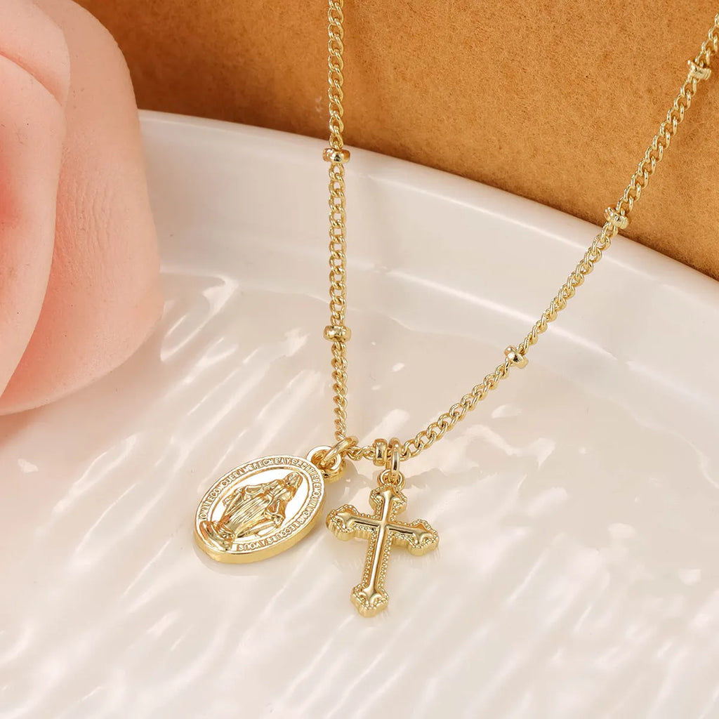 Gold-coloured geometric Virgin Mary and cross pendant necklace on a chain.