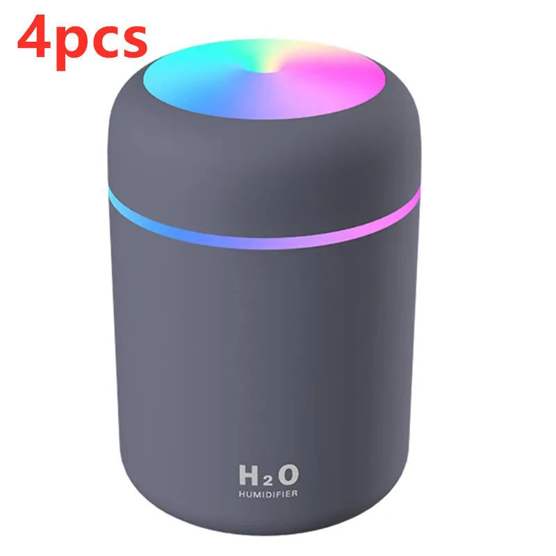 Pink USB desktop humidifier with LED lights and water tank on a wooden desk.