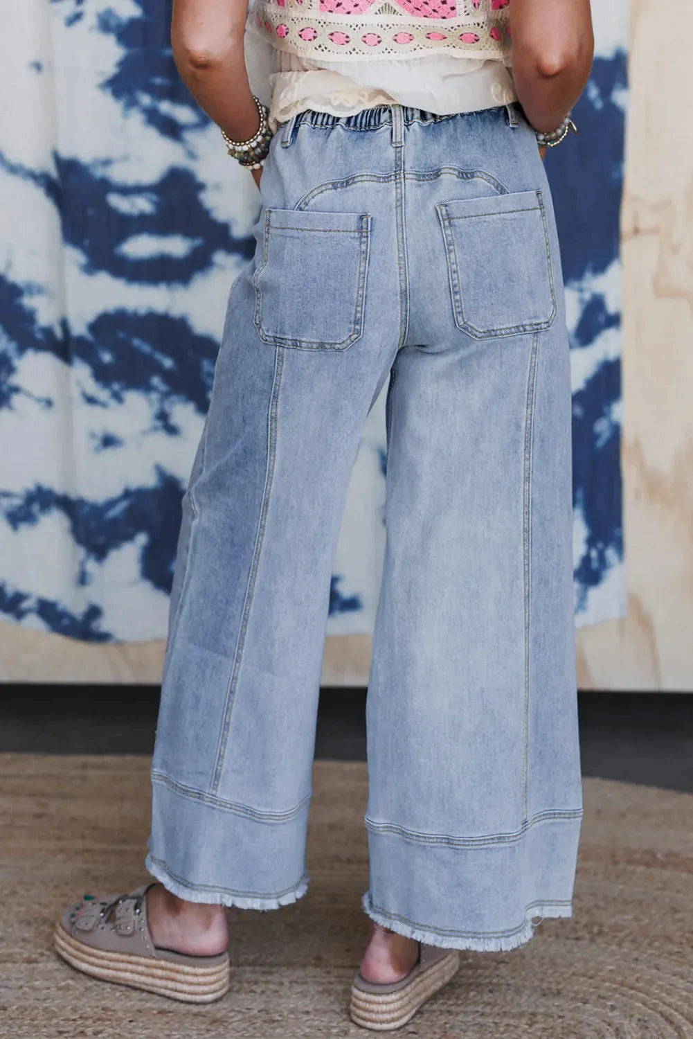 Beau blue wide leg denim trousers with drawstring waist and raw hem detail laid flat