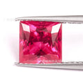 Loose cultivated pigeon blood red ruby gemstone in a princess cut on a grey background.