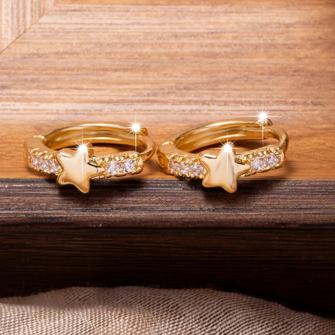 Gold copper five-pointed star earrings with inlaid zircon stones on a neutral background