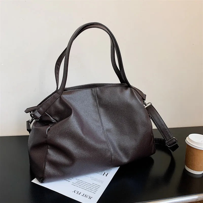 Large soft surface black messenger bag with soft handle and long shoulder strap on a table
