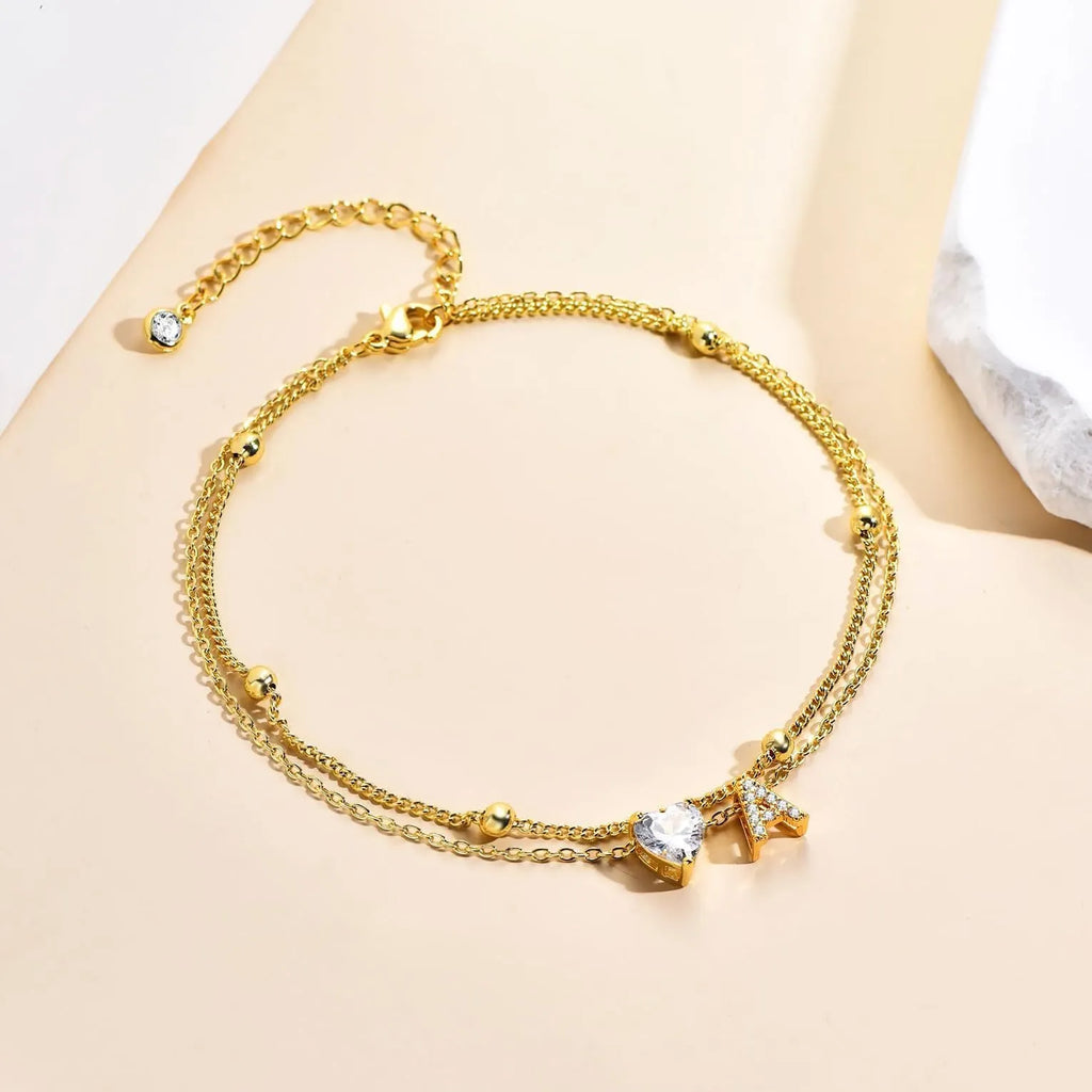 Layered copper anklet with zircon inlaid letter charm, bead zircon style, on a light background.