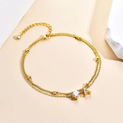 Layered copper anklet with zircon inlaid letter charm, bead zircon style, on a light background.