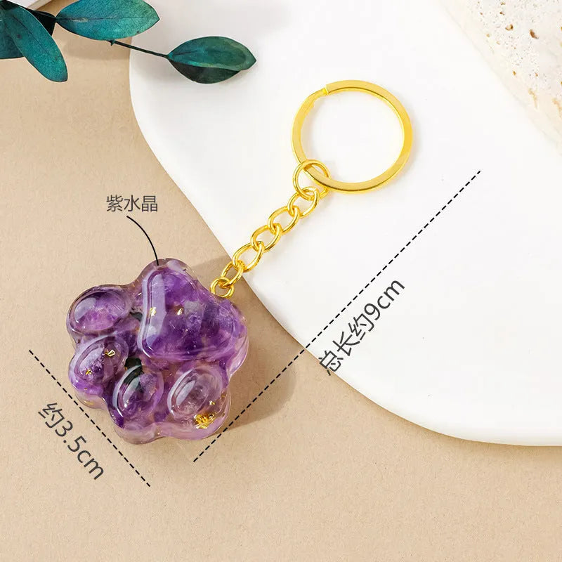 Small natural crystal cat's paw charm on a keyring, showing colour options including pink, red, blue, and purple gemstones.
