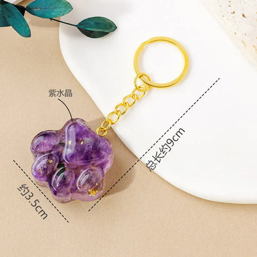 Small natural crystal cat's paw charm on a keyring, showing colour options including pink, red, blue, and purple gemstones.