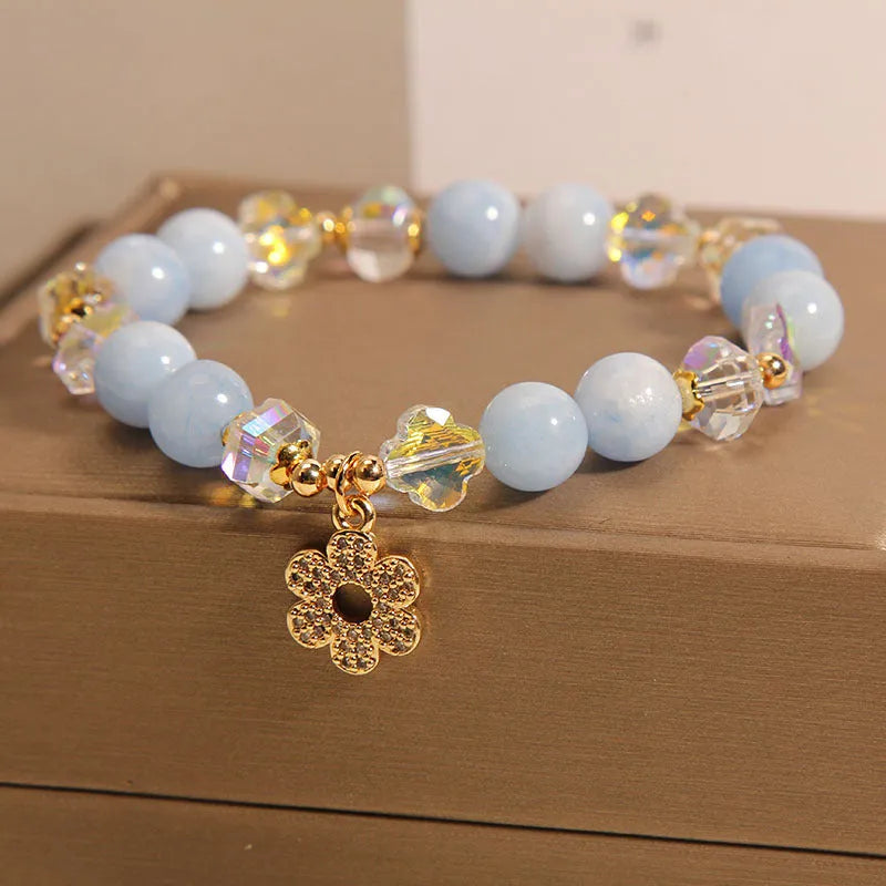 Women's bracelet with aquamarine crystal clover charm and white pearl details on a light background.