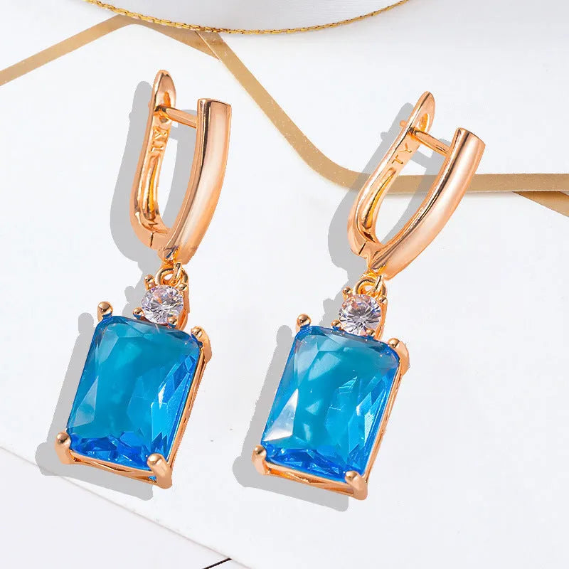 A pair of square-shaped gold-coloured electroplated earrings on a flat surface.