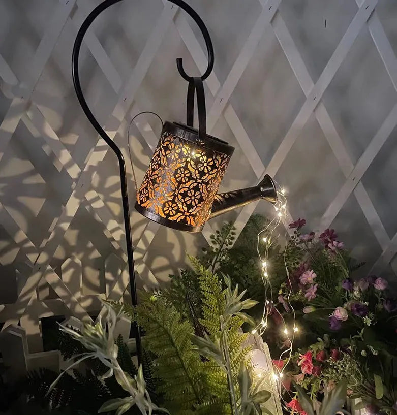 Enchanted watering can solar lamp with warm white star-shaped LED lights in a garden setting