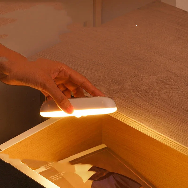 Fully automatic unplugged bedside night light for dormitory with magnetic base, USB rechargeable, showing yellow light mode on a dark bedside table