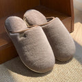 Solid colour PVC plush winter house slippers on a wooden floor.