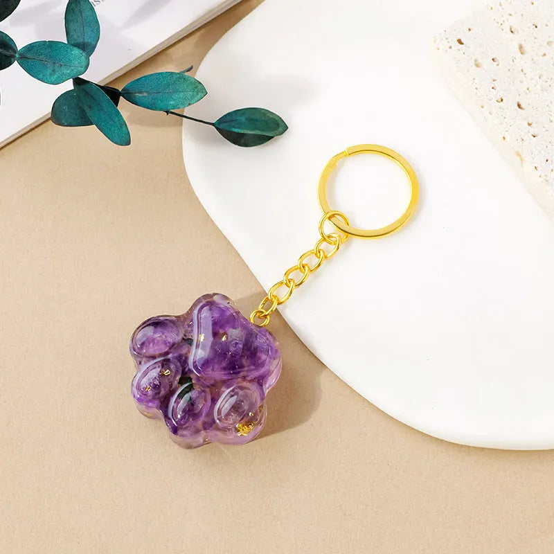 Small natural crystal cat's paw charm on a keyring, showing colour options including pink, red, blue, and purple gemstones.