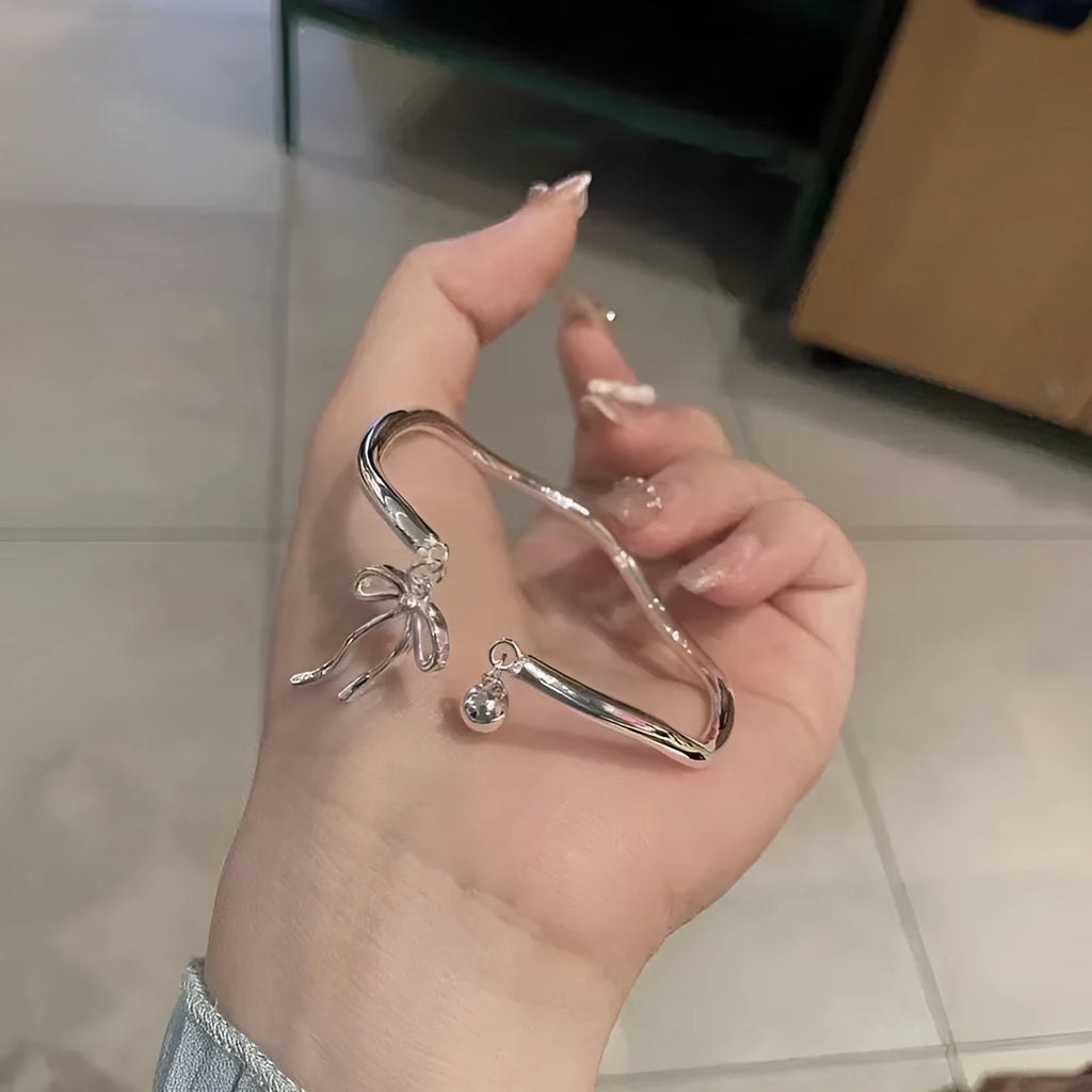 Silver tone adjustable bracelet with a bow charm on a white background.
