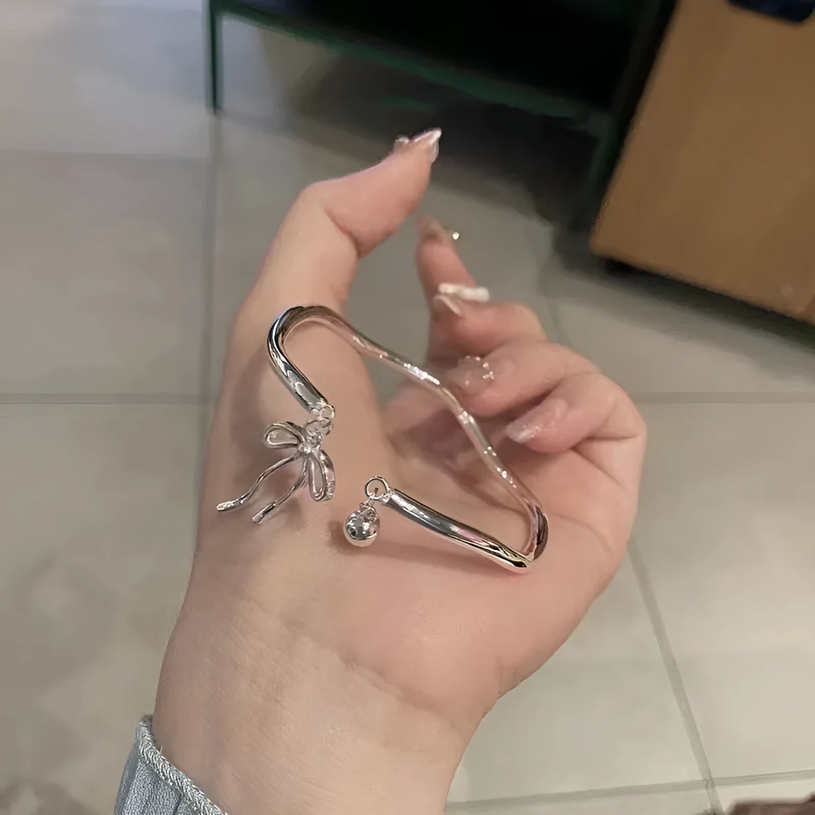 Silver tone adjustable bracelet with a bow charm on a white background.